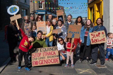 A group of people, including children, hold up signs protesting fossil fuels and climate change on a street decorated with bunting.