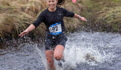 A runner wearing a race bib numbered 92 splashes through a stream during an outdoor cross-country event.