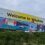 Large "Welcome to Whalsay" sign with colourful illustrations of local wildlife, buildings, and a boat, placed on a grassy hillside under a cloudy sky.