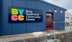 Blue building with a sign that reads “BYCC Brae Youth and Community Centre” and a red door.