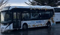 A white Enviro100EV battery-electric bus parked on wet tarmac, decorated with toast-slice graphics and the text "Powerful enough to make